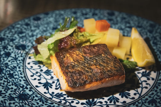 Grilled salmon fillet on a patterned plate with salad and lemon wedges, symbolizing the use of salmon DNA in skincare treatments.